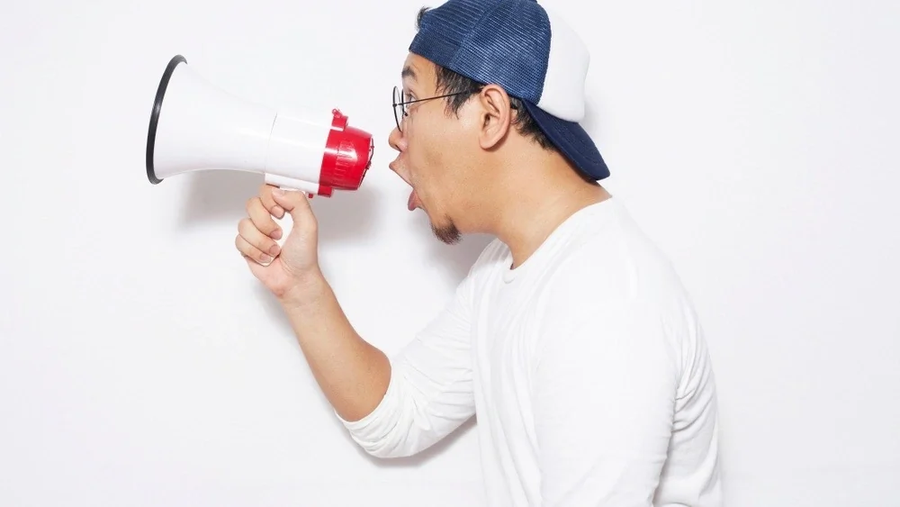 Young Asian sman wearing white shirt shouting with megaphone, angry expression. Close up body portrait, side view; Shutterstock ID 1246487137; Purchase Order: ; Job: ; Client/Licensee: decrypt media; Other: