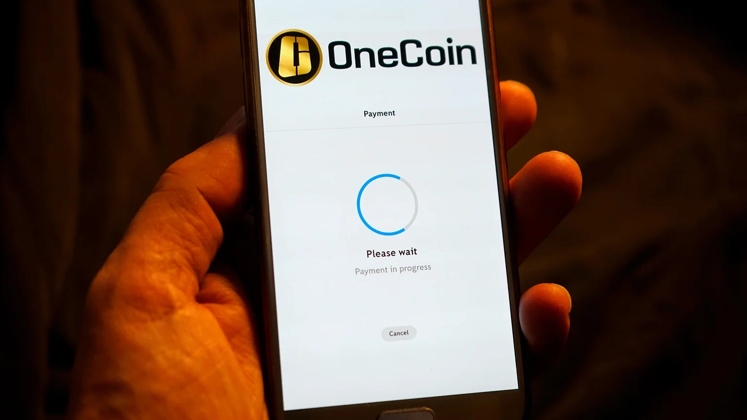 Hand holding smartphone with OneCoin logo