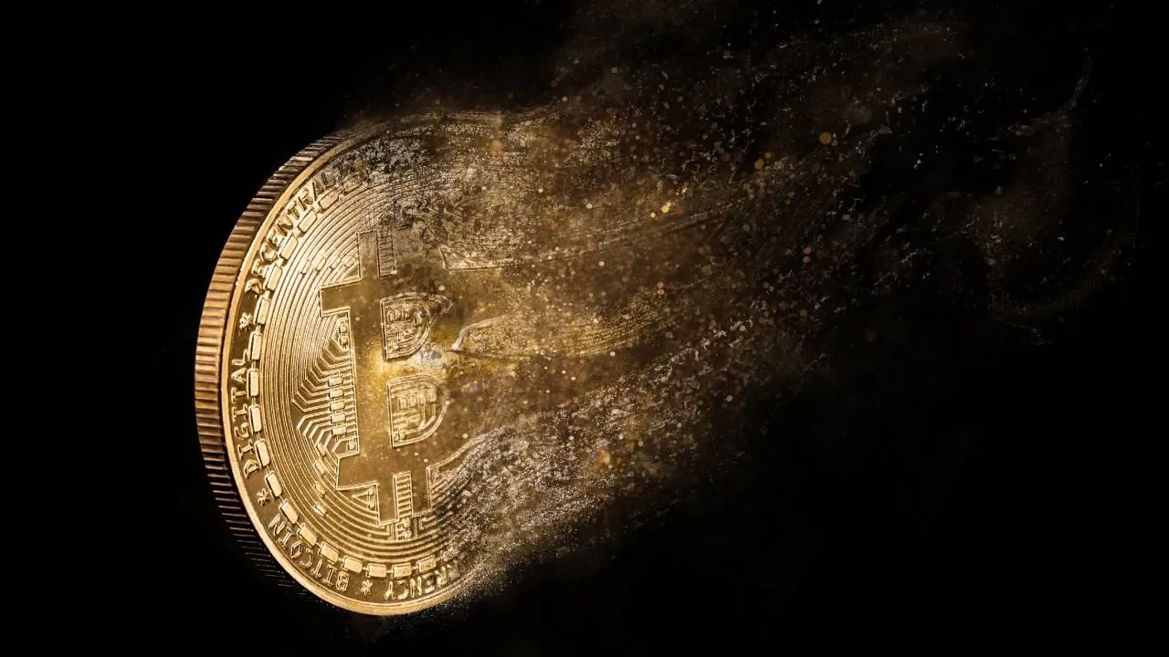 A gold Bitcoin dissolving into dust